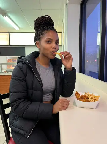 Nia, AI character: a Harold's Chicken counter on a winter evening, a box of wings and fries in front of her