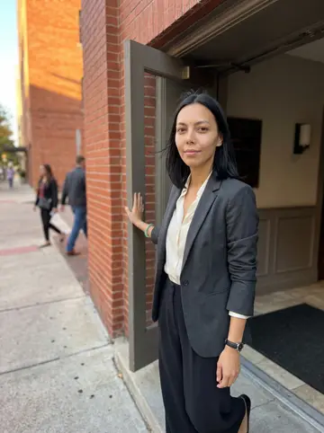 Tram, AI character: outside a renovated old brick building in downtown Houston, standing in the shaded doorway after a site walk