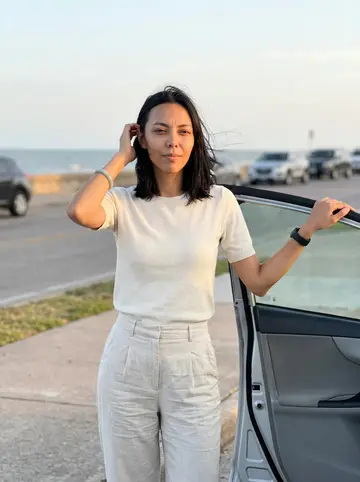 Tram, AI character: near the Galveston seawall at golden hour, standing by the open passenger door after a short drive from…
