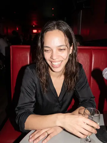 Karine, AI character: a small Tuesday karaoke bar in Montréal, red vinyl booth behind her and a microphone stand nearby