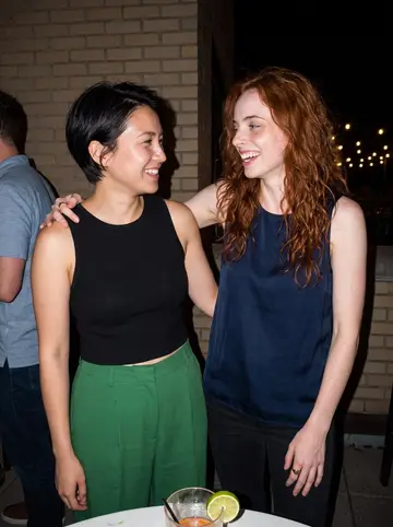 Isla, AI character: a crowded rooftop patio bar in Boston with string lights and a friend's shoulder at the edge of the frame,…