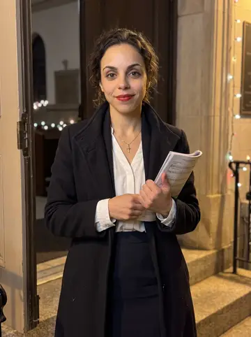 Jéssica, AI character: outside Our Lady of Fatima after evening choir rehearsal in Newark, with holiday lights along the church…