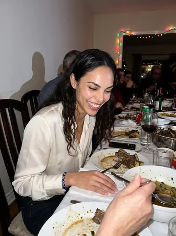 Antigoni, AI character: her yiayia's crowded dining room during Sunday lamb with relatives, plates and serving bowls all over the…
