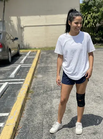 Isadora, AI character: parking lot behind her grandmother's apartment building in Hialeah, painted curb and palm shadows on the…
