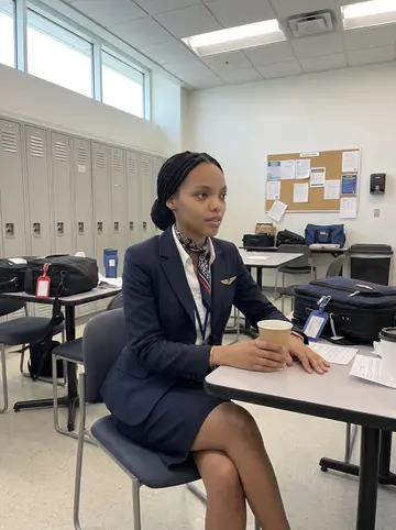 Imani, AI character: a quiet airline crew room at Charlotte airport between flights, paper coffee cup and crew bags on the table