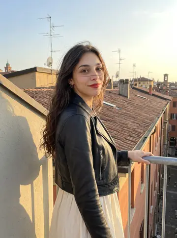 Alessandra, AI character: a rooftop in Bologna near Via del Pratello at golden hour, low terracotta roofs and antennas behind her