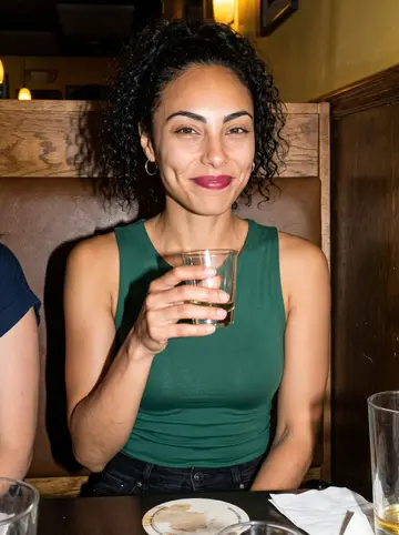 Bruna, AI character: a Brazilian bar in Somerville after a roda, friends cropped at the edges of the booth