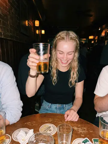 Viktoria, AI character: a small corner table at a neighborhood bar after her beer hall shift, friends cropped out on both sides