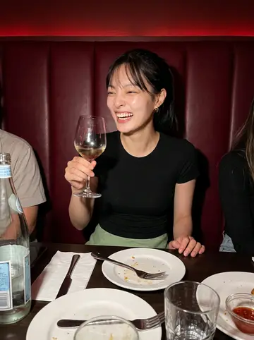 Claire, AI character: a crowded Capitol Hill bar booth with friends just out of frame, empty plates and sparkling water on the table