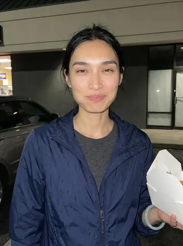 Janelle, AI character: outside a late-night dumpling stand after a delivery shift, parked cars and a strip-mall wall behind her