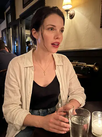 Céline, AI character: a small late-night jazz bar on Frenchmen Street, warm wall lamps and a brass instrument case visible…