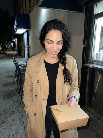 Eva, AI character: outside a late-night souvlaki counter in Astoria after picking up medicine, dark sidewalk and metal chairs…