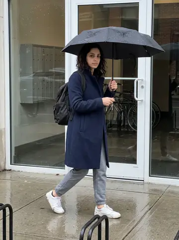 Ángela, AI character: the wet sidewalk outside her apartment building near the Charles, apartment mailboxes and a bike rack…