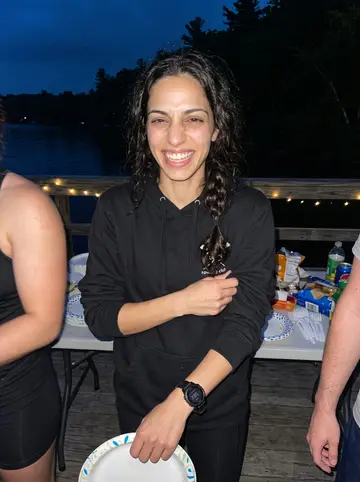 Ángela, AI character: a humid evening on a dock after a rowing club cookout, cropped teammates at the edges and paper plates on…