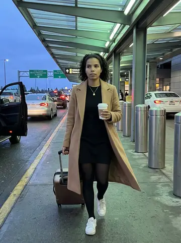 Ngozi, AI character: SeaTac arrivals curb at blue hour, rolling suitcase beside her and traffic lights blurred in the background