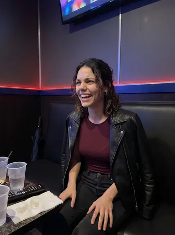 Chelsea, AI character: a small private karaoke room in Chicago after rain, vinyl booth seat, cups on the table, colored wall…