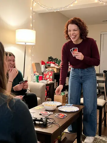 Brooklyn, AI character: friend's apartment holiday game night in Cincinnati, string lights and cards scattered on the coffee table