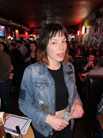Kayla, AI character: the same Denver dive bar late on trivia night, crowded booths behind her and a small stack of answer…