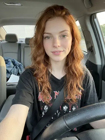 Shannon, AI character: parked in her car in Raleigh after work, dashboard visible with a notebook of jokes on the passenger seat