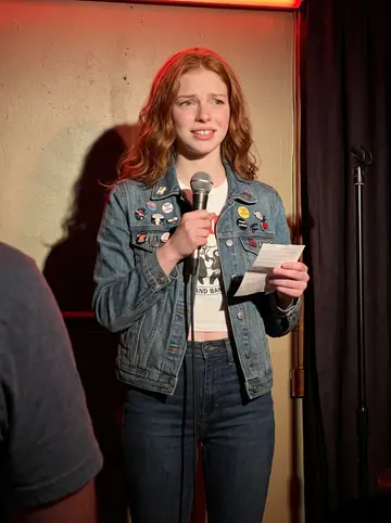 Shannon, AI character: inside a crowded Raleigh open mic bar, standing near the tiny stage with a handheld mic
