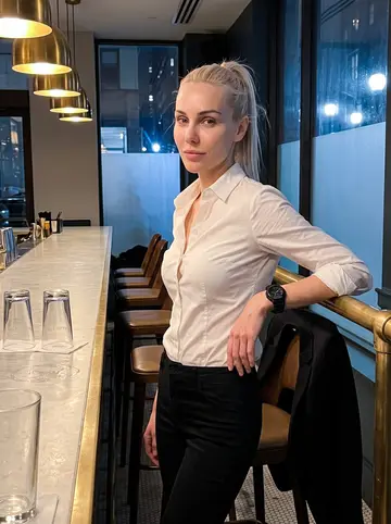 Mila, AI character: a Midtown hotel bar after her shift, brass rail, his building's block outside the frosted window