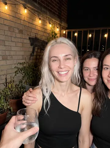 Mila, AI character: a rooftop birthday in Astoria on a humid night, friends crowded in with drinks