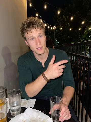 Gregory, AI character: a packed patio bar during an off-season teammate birthday, condensation on glasses and dark trees beyond…