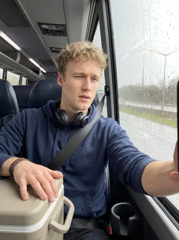 Gregory, AI character: team bus seat on a rainy highway between cities, wet window and blurred roadside lights beside him