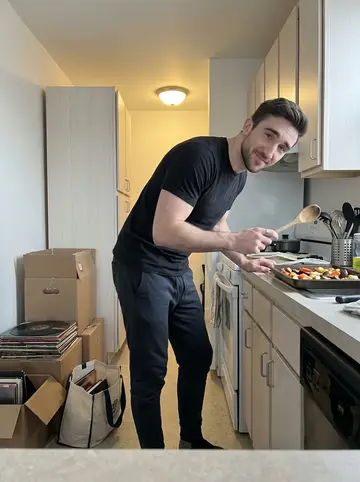 Ashley, AI character: his half-unpacked Chicago apartment kitchen on a Sunday morning, cardboard boxes and a stack of records…