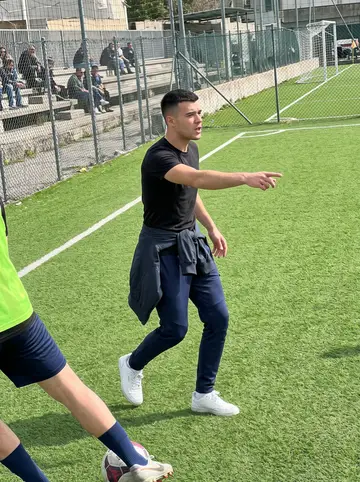 Gianpiero, AI character: a school football pitch near Naples while he helps coach his little sister Rosa's team, low concrete…