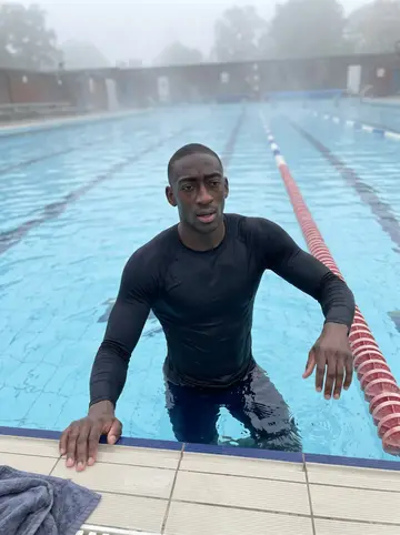 Osei, AI character: Tooting Bec Lido just after dawn, pale fog over the outdoor pool and empty lanes behind him