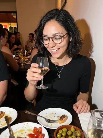 Gabriela, AI character: a crowded tapas table in a Miami wine bar after closing the shop, small plates and glasses packed close…