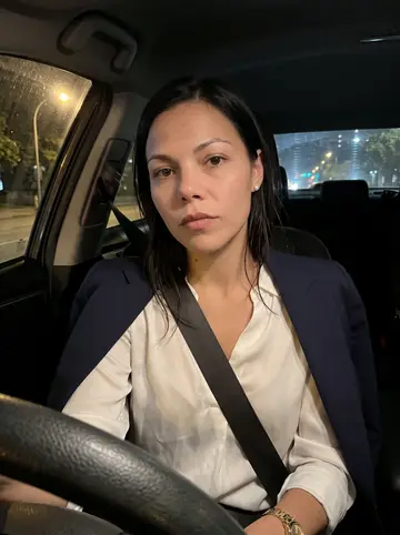 Natalie, AI character: parked along Memorial Drive after a late meeting, downtown Houston lights faint through the windshield