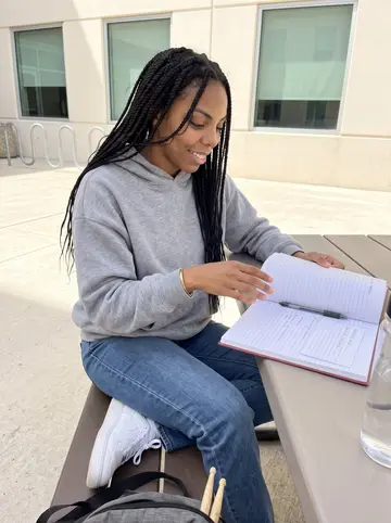 Onyinye, AI character: a shaded table outside a Houston campus science building between pre-med classes