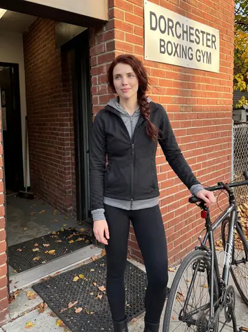 Donna, AI character: outside her Dorchester boxing gym at golden hour, her road bike leaned against the brick wall beside her