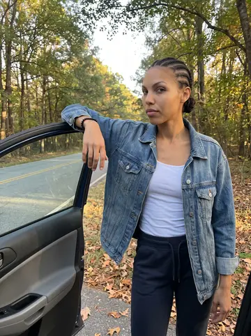 Amara, AI character: a quiet tree-lined road outside Atlanta near a parked dark-blue compact SUV, late afternoon practice drive…