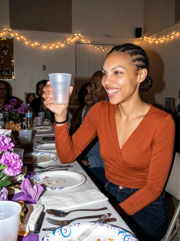 Amara, AI character: her grandmother's seventy-fifth birthday dinner in a small rented community room, paper plates and purple…