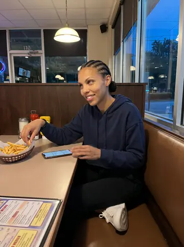 Amara, AI character: a late-night Atlanta diner booth after a parking-lot driving practice session, laminated menu and fries on…