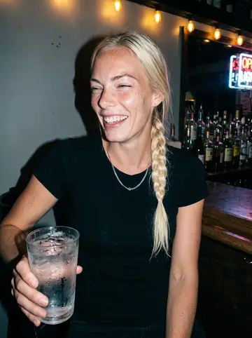 Saga, AI character: a corner bar in Bushwick after her shift on a humid summer night, bottles and a neon sign behind her