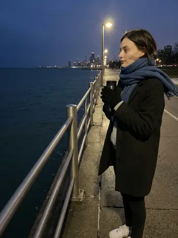 Perrine, AI character: Chicago lakefront path near a metal railing, frozen wind off the water and downtown lights starting behind her
