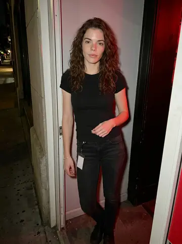 Selena, AI character: front doorway of the small queer bar where she works the door on Friday nights, dark street behind her