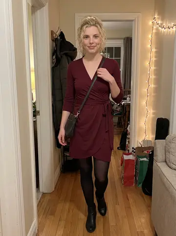 Amy, AI character: her aunt's living room doorway before a family holiday party, warm string lights and coats on hooks in the…