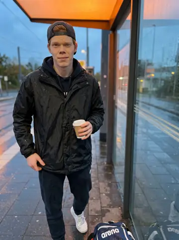 Patrick, AI character: wet tram stop outside Cologne Messe after practice, arena bag at his feet