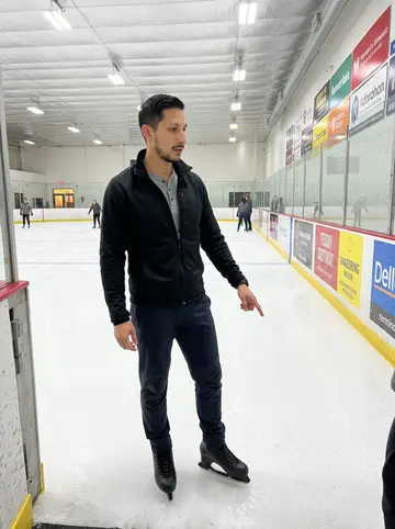 Elliot, AI character: indoor rink during a Tuesday-night adult beginner skating class, all skaters are adults, blue line and…