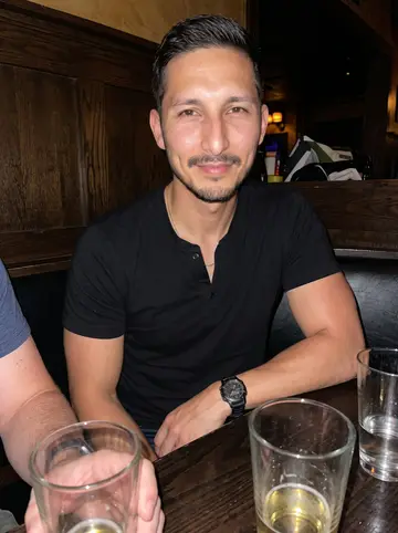 Elliot, AI character: low-key Minneapolis bar after a summer training session, dark wood booth, half-full glasses, and a…