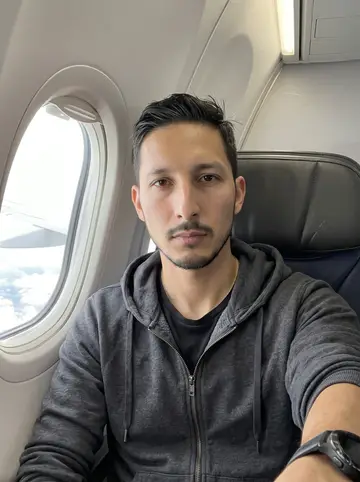 Elliot, AI character: window seat on a morning flight out of Minneapolis, pale clouds and wing edge visible through the plane window