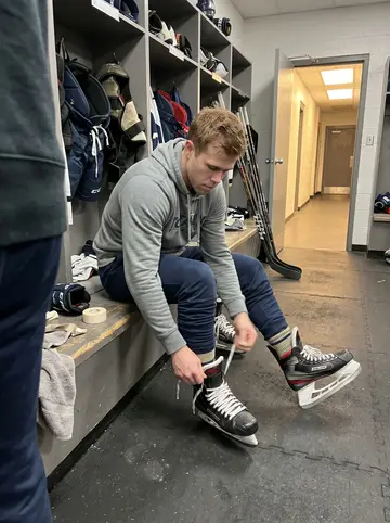 Cian, AI character: team locker room after a late practice, rubber floor mats, open gear stalls, sticks stacked by the wall