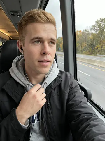 Cian, AI character: team bus rolling out before an away game, grey highway and autumn trees through the window