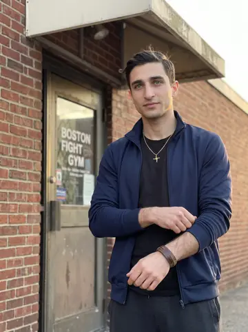 Jonny, AI character: outside his Boston fight gym just after evening training, brick wall and gym door behind him