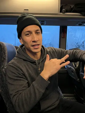 Yoandy, AI character: team bus parked outside a small away-game arena at blue hour, frosty window behind his seat